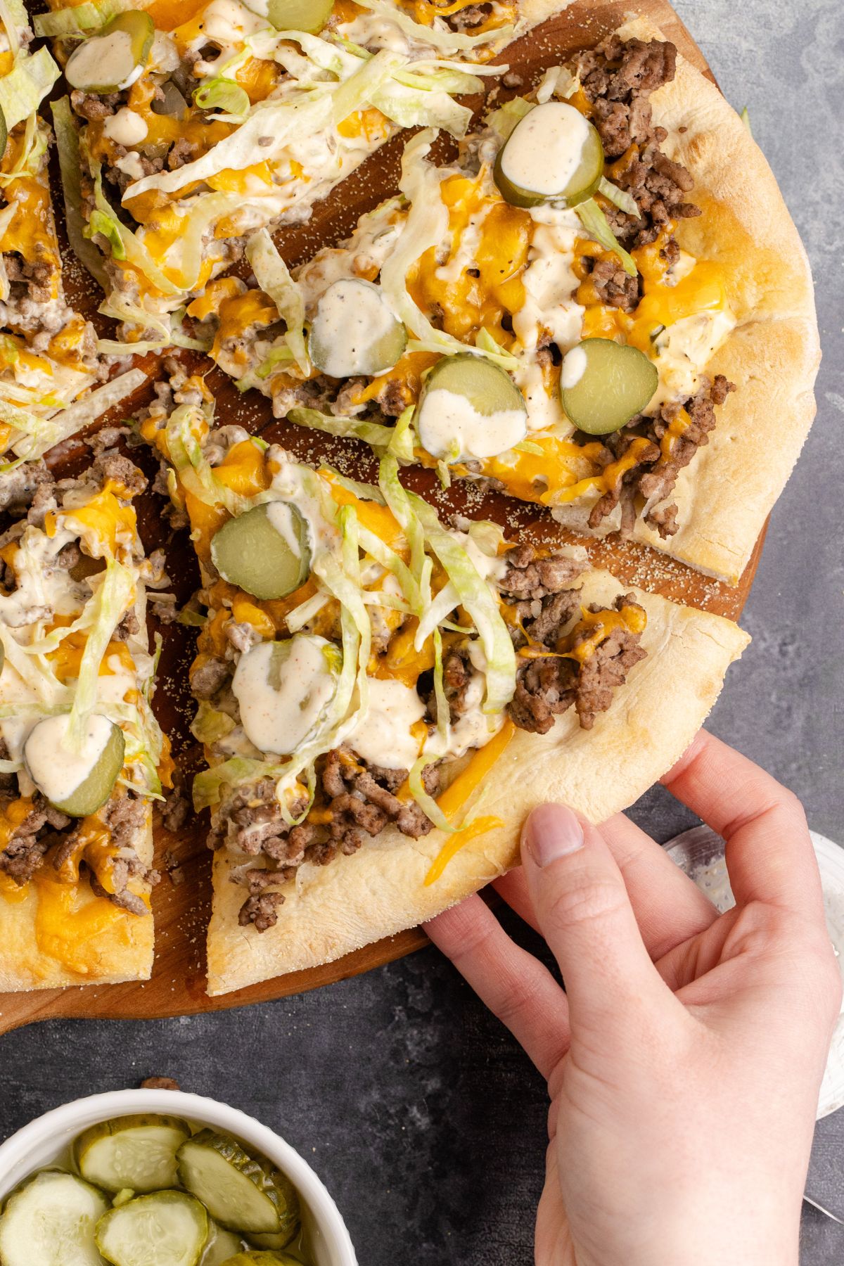 A hand pulling a slice of Big Mac pizza from the pie cut into slices.