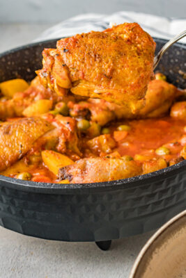A spoon lifting a cooked chicken thigh, the Pollo con papas is complete.
