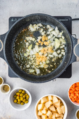 Diced onions and garlic cooking inside a skillet.