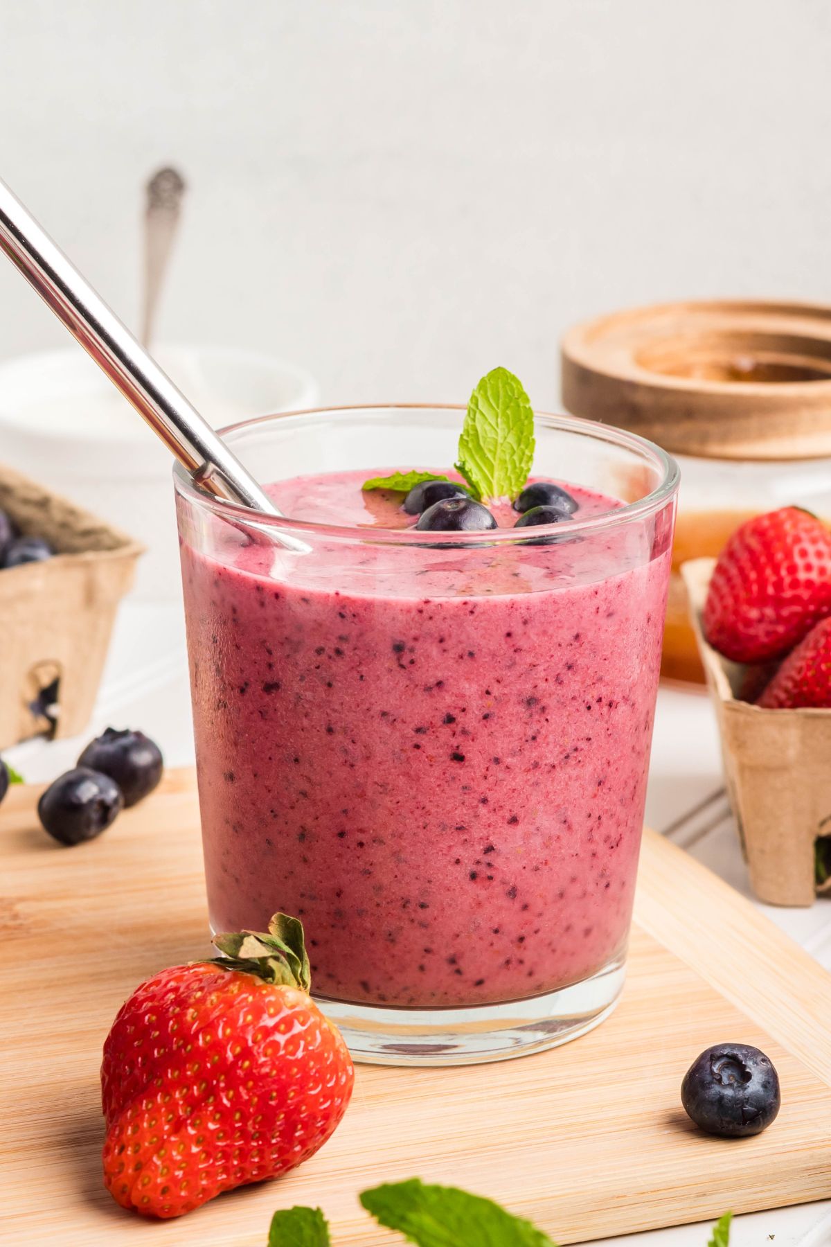 Berry smoothie in a glass garnished with some blueberries, mint and a straw.