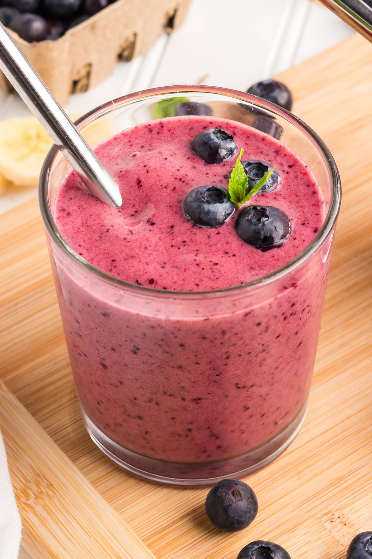 Smoothie with berries in a glass with blueberries, mint, and a straw.