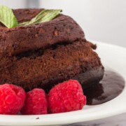 Lava cake with chocolate sauce surrounding the cake on a plate with raspberries.