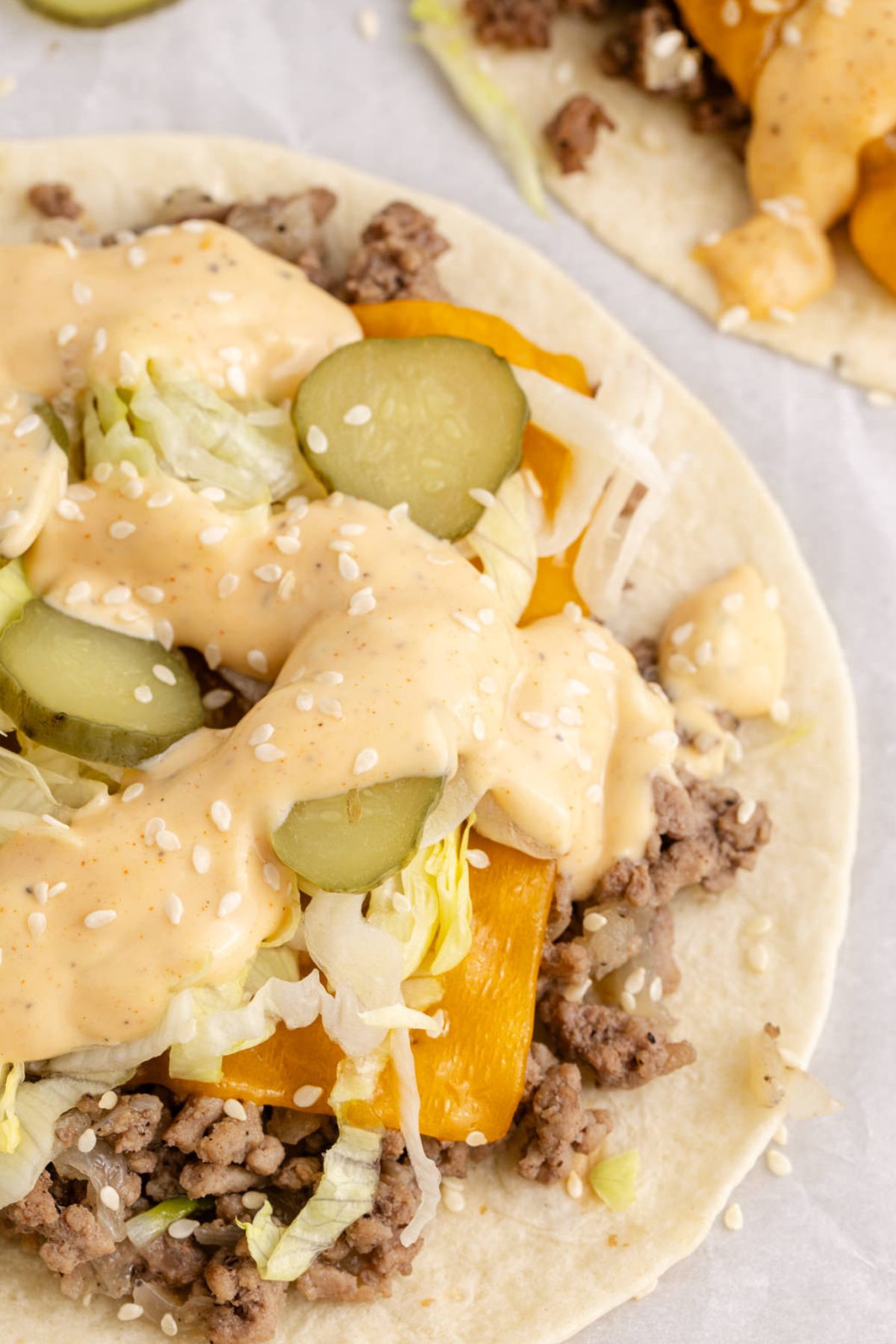 Tacos with cheese, pickle, lettuce, and sauce over beef and sesame seed on top.