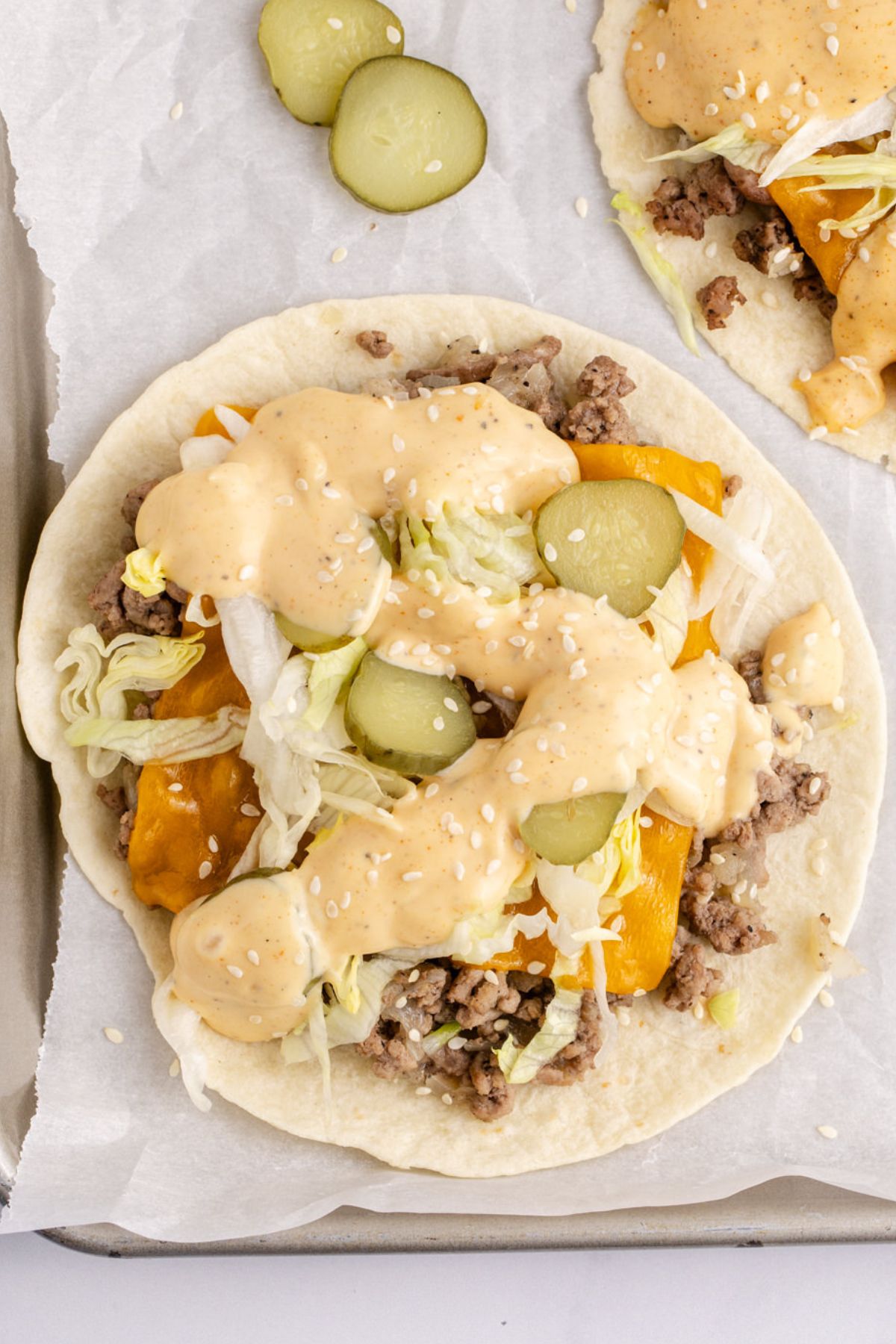Cheese, pickle slices, lettuce, and a good drizzle of sauce over beef on the taco shell.