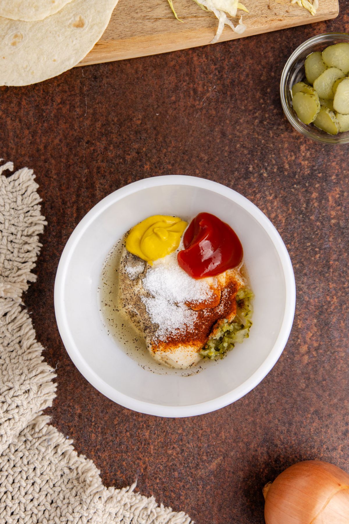 Mayo, ketchup, and mustard, pickles, vinegar and spices in a bowl.