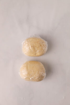 Dough divided in half and wrapped with plastic wrap.