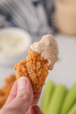 Fingers holding a chicken nugget dipped into buffalo ranch sauce.