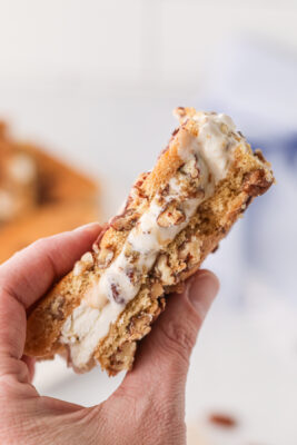 A hand holding an ice cream cookie sandwich over the table to take a bite.