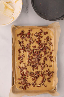 Pecans are sprinkled over the top of the cookie crust before baking in the oven.