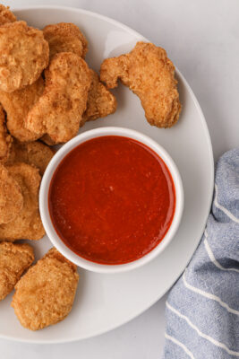 Bowl of McDonald's buffalo sauce served on a plate with chicken nuggets.