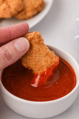 A hand dipping food into a bowl of McDonald's buffalo sauce.