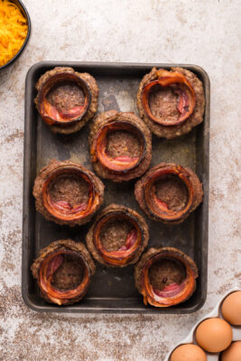 Bacon rings placed inside the sausage bowls. The sausage bowls are placed on a rimmed baking sheet.