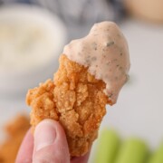 A chicken tender piece with buffalo ranch sauce being held up.