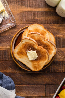 Three thick slices of toasted bread on a plate. Topmost slice has a slice of butter.