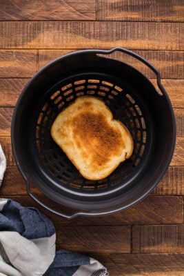 Thick slice of toast placed inside an air fryer basket.