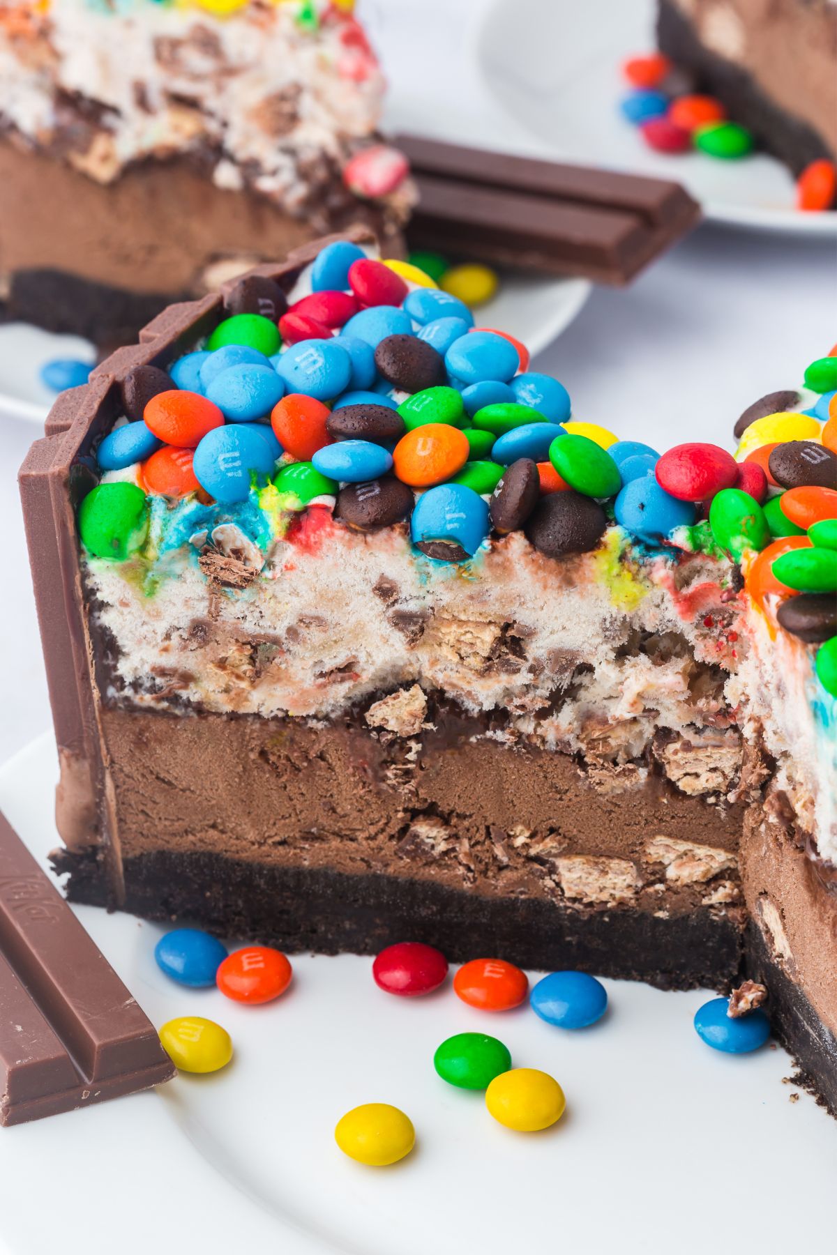 A slice of ice cream cake with kit kat and m&ms on top.