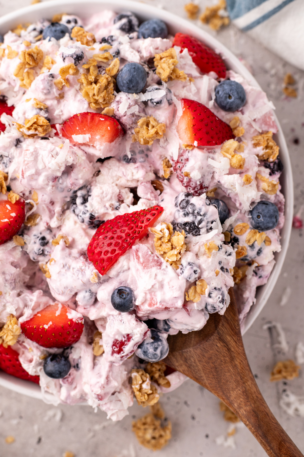 Cheesecake with fruit and granola being scooped with a wooden spoon.