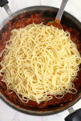 Cooked spaghetti noodles added to the top of tomato sauce in the skillet.