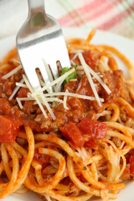 Closeup photo of school cafeteria spaghetti in a white bowl. A fork is digging into the spaghetti.