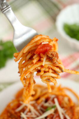 Closeup photo of a forkful of spaghetti. The fork is held above a bowl of spaghetti.