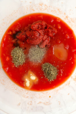 Diced tomatoes and juice from tomatoes, tomato paste, sugar, worcestershire sauce, oregano, basil, garlic powder, salt, and pepper added to a large mixing bowl.