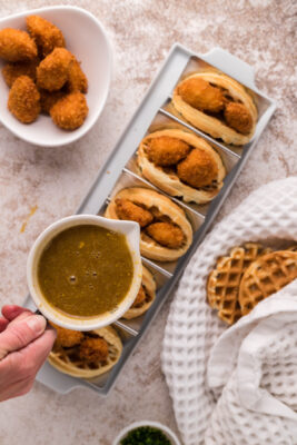 Pouring maple mustard syrup onto chicken waffle tacos.