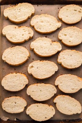 Overhead photo of baguette slices placed on a baking sheet with parchment paper.