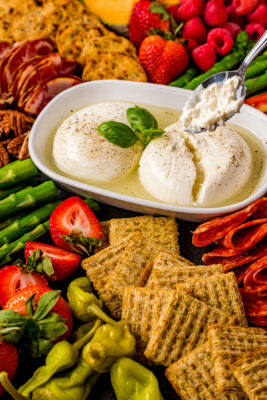 Closeup photo of the burrata cheese board. A spoonful of Burrata cheese is hovering over the container of burrata cheese.