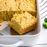 Broccoli cornbread with cheese in pan being lifted out.