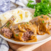 A plate with mashed potatoes and two Salisbury steaks topped with brown gravy.