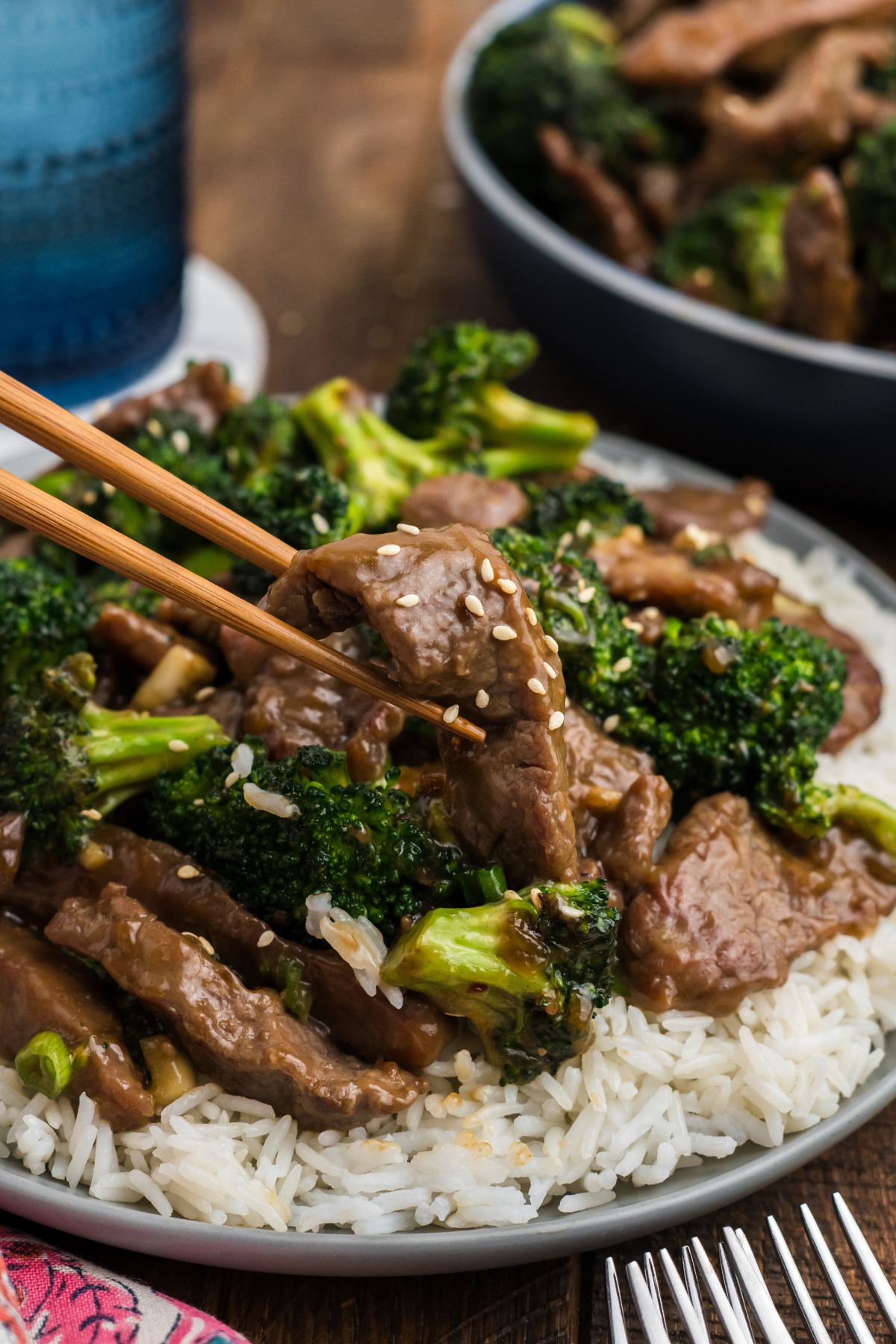A plate of beef with garlic sauce and chopsticks picking up a piece of beef with sesame seeds on it.