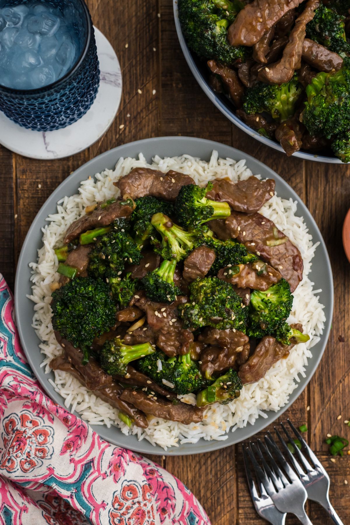 Beef with broccoli over a plate of white rice and sesame seeds over top.