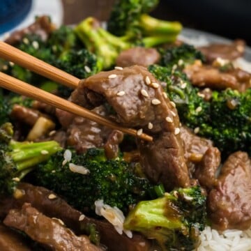 Chopsticks holding a piece of beef with garlic sauce.