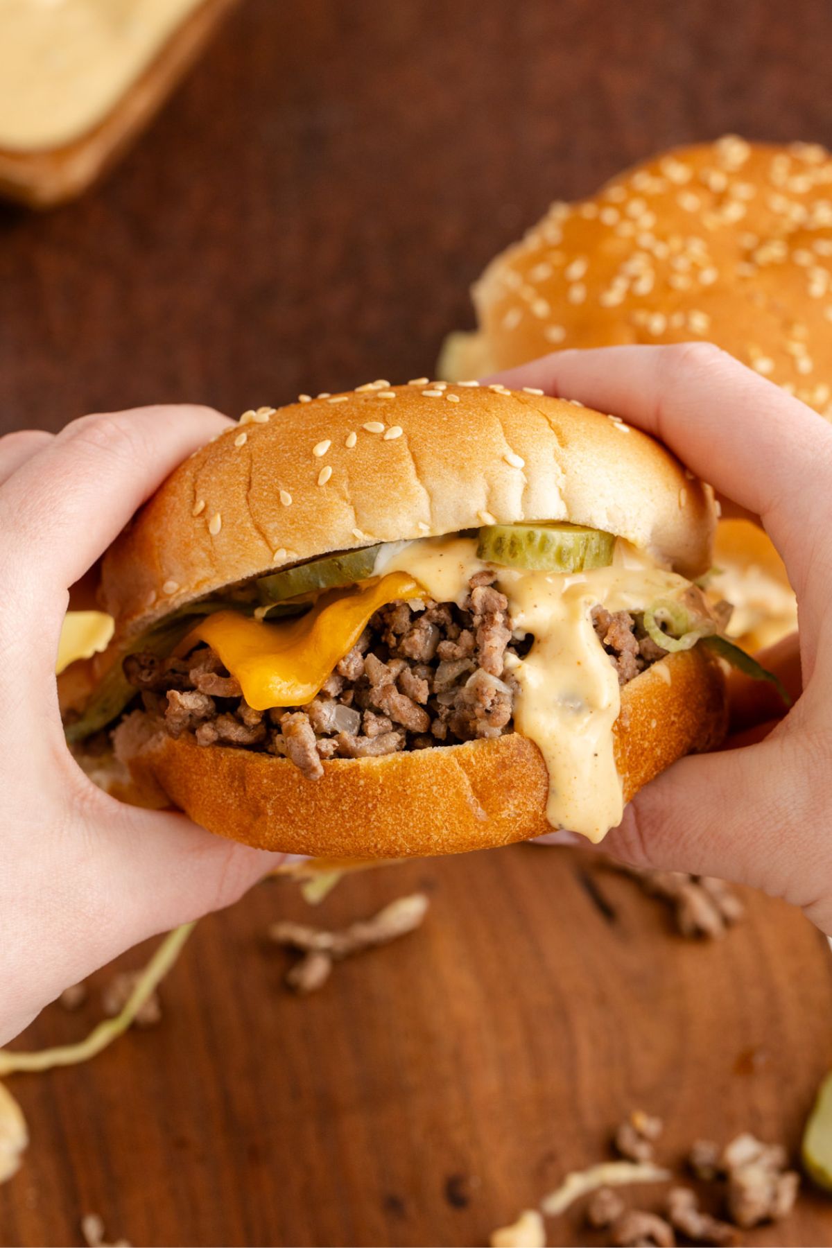 Hands holding a loppy Joe with cheese, pickles and big mac sauce on a bun.