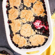 A baking dish of blueberry cobbler with cake mix on the counter with a portion missing.