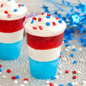 red white and blue jello cups in a clear plastic cup with cool whip and sprinkles on counter