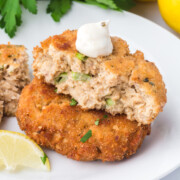 Old-Fashioned Salmon Patties on top of each other with the top one missing a few bites with a dollop of sour cream.
