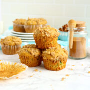 Three pumpkin zucchini muffins piled on top of each other on a white counter.