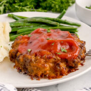A mini meatloaf with a side of green beans and mashed potatoes.