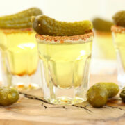 Pickle shots on a wooden serving board. Each shot is rimmed with Tajin and garnished with a baby dill pickle.