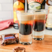Two snickers shots on the table with a candy bar in the package next to it.