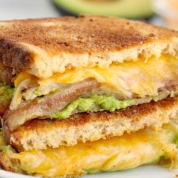 Grilled cheese sandwich with avocado and bacon on a white plate.