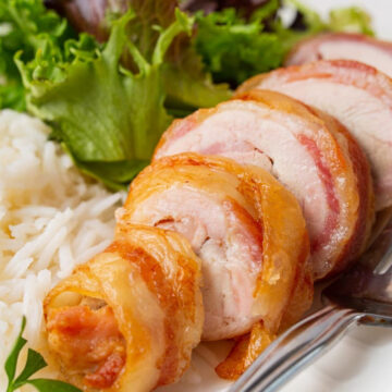 Sliced bacon-wrapped chicken thighs served with white rice and a side of fresh green salad on a white plate.