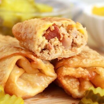 Sliced fried egg rools filled with cheese and meat, served with pickles and tomato sauce on a wooden board.