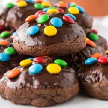 Chocolate brownie cookies topped with melted chocolate and colorful candy pieces on a white plate.
