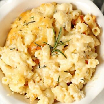 A bowl of cheesy macaroni and cheese garnished with rosemary, placed on a white napkin.