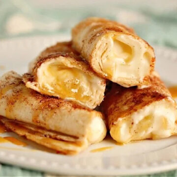 A stack of flour tortillas filled with cream, sprinkled with cinnamon, and drizzled with caramel sauce on a white plate.