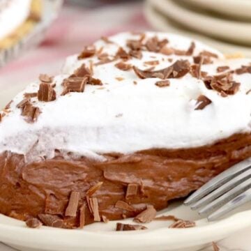 A slice of old-fashioned chocolate pie topped with whipped cream and chocolate shavings on a white plate with a fork.