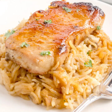 pork chop from easy pork chop recipes served on a bed of seasoned rice with parsley garnish on a white plate, accompanied by a fork.