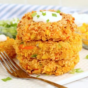 Three stacked potato fritters topped with sour cream and garnished with green onions on a white plate, with a fork on the side.